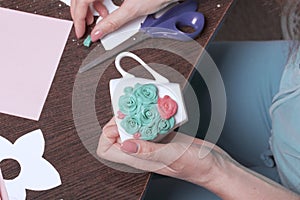 Crafts from polymer clay. A woman sticks a gummed polymer clay flower to a cup. Mug decorated with stucco made of polymer clay