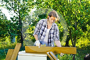 Crafts woman in protective glasses and gloves doing woodwork in summer garden