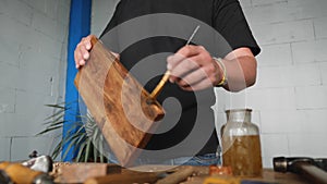 The craftsman applies the wood impregnation to the walnut board with a brush. artisan makes a tray. vagatabon