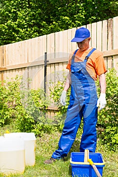 Craftsman in blue overalls and orange T-short looking at paint cans and bucket