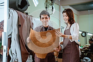 craftsman and craftswoman in apron inspect leather tanned sheets