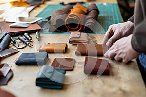 Craftsman hands laying out leatherwork on wooden table at leather workshop. Handwork accessories
