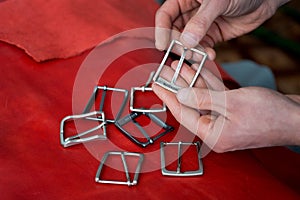 Craftsman hands and metal buckles top view on red leather background. Accessories for