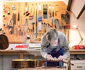 Craftsman in his workshop leveling the frets of a guitar