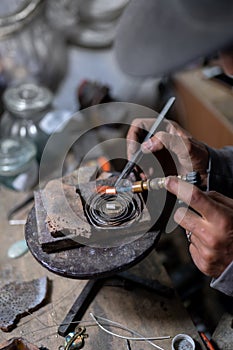 A craftsman jeweler is using a blowtorch to create a metal cilinder for a bracelet