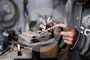 A craftsman jeweler is using a blowtorch to create a metal cilinder for a bracelet