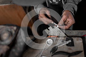 A craftsman jeweler is using a file tool to create a metal cilinder for a bracelet