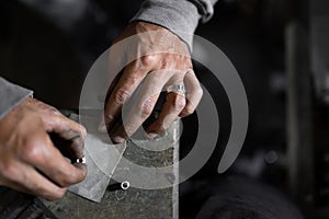 A craftsman jeweler is using a sandpaper to tile a metal cilinder for a bracelet