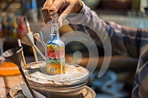 Craftsman makes souvenirs in a bottle using colored sand