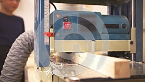 Craftsman passes a wooden beam through the carpentry grinding machine, teen boy standing near and watching