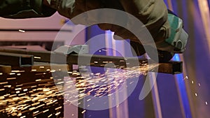 Craftsman in protective gloves working with grinder at industrial plant, man grinding iron detail, sparks flying around.