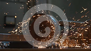 Craftsman in protective gloves working with grinder at industrial plant, man grinding iron detail, sparks flying around