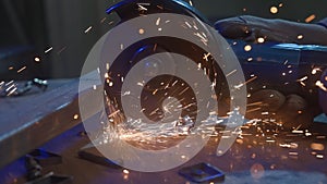 Craftsman in protective gloves working with grinder at industrial plant, man grinding iron detail, sparks flying around