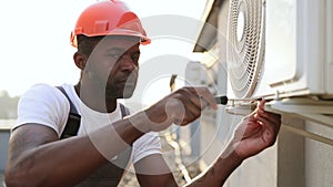 Craftsman repairing air conditioner with screwdriver on roof