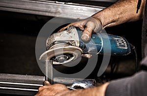 Craftsman sawing metal with disk grinder in workshop. Grinding metal.