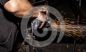 Craftsman sawing metal with disk grinder in workshop. Grinding metal with sparks flying