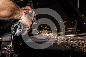 Craftsman sawing metal with disk grinder in workshop. Grinding metal with sparks flying