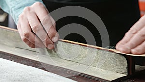 A craftsman is sharpening the edges of a belt. The leather master is making a belt