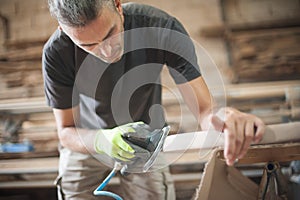 Craftsman using electric sander, to smoothen the wood texture photo