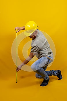 Craftsman worker with hard hat is measuring with a tape measure isolated on yellow background