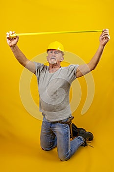 Craftsman worker with hard hat is measuring with a tape measure isolated on yellow background