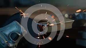 Craftsman working with grinder at industrial plant, man grinding edge of iron detail, sparks flying around and falling