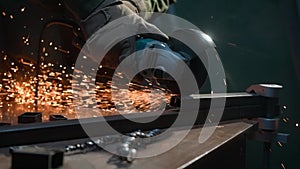 Craftsman working with grinder at industrial plant, man grinding edge of iron detail, sparks flying around and falling