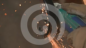 Craftsman working with grinder at industrial plant, man grinding edge of iron detail, sparks flying around and falling