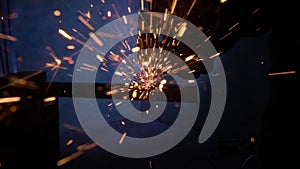 Craftsman working with grinder at industrial plant, man grinding iron detail, sparks flying around and falling on the