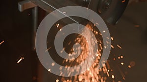 Craftsman working with grinder at industrial plant, man grinding iron detail, sparks flying around and falling on the