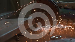 Craftsman working with grinder at industrial plant, man grinding iron detail, sparks flying around and falling on the