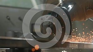 Craftsman working with grinder at industrial plant, man grinding iron detail, sparks flying around and falling on the