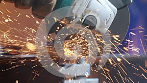 Craftsman working with grinder at industrial plant, man grinding iron detail, sparks flying around and falling on the