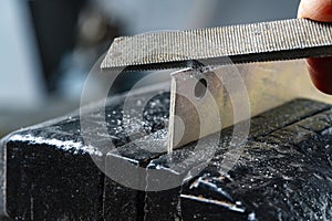 Craftsman works on small piece of metal with metal file gripped in vise on workbench table in garage workshop, do it yourself