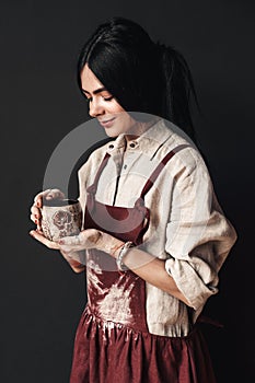 Craftsperson Concept. Young woman artist standing isolated on dark with cup smiling happy
