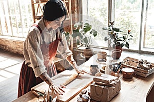 Craftsperson Concept. Young woman making pottery at creative studio standing rolling clay joyful in daylight