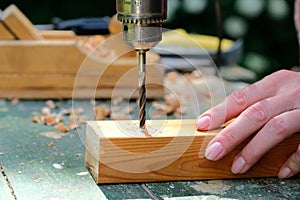 Craftswoman carpenter drilling a wooden plank with drill machine, closeup view. Woodworking, DIY concept