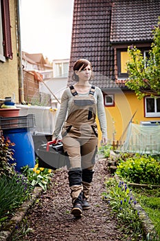 a craftswoman carrying a toolbox and walking through a garden