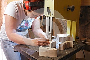 Craftswoman is cutting a wood toy cars workpiece from wood with bandsaw.