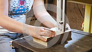 Craftswoman is cutting a wood toy cars workpiece from wood with bandsaw. Hands close-up.