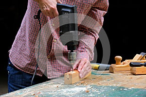 Craftswoman drilling a hole with an electric drill machine in wooden plank, closeup view. Concept of joiner`s shop and woodworkin