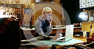 Craftswoman using laptop while talking on mobile phone