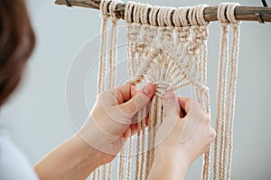 Craftswoman weving ropes, creating a macrame banner. from behind