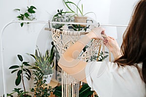 Craftswoman working on unfinished section of a macrame piece at home greenhouse