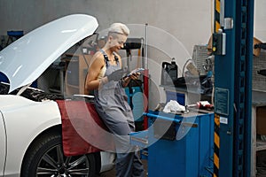 Craftswoman at workplace in auto repair shop is chatting on phone