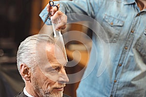 Crafty master combing hair of the aged client in the salon