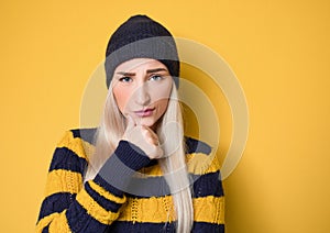 Crafty young woman thinking. Closeup portrait of smart person, model wearing woolen cap and sweater,  on yellow background
