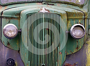 Close up of the front of an old abandoned rusting green truck covered in moss