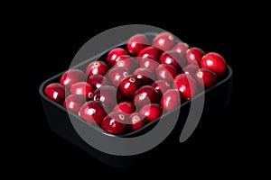 Fresh large cranberries, in a black bowl, isolated on black background