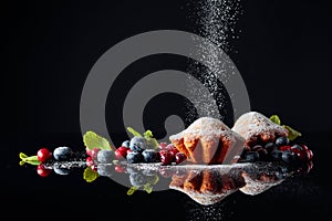 Cranberry and blueberry muffins sprinkled with sugar powder on a black reflective background. Muffins with berries and mint